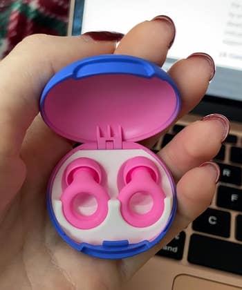 reviewer's hand holding pink Loop earbuds in its colorful case