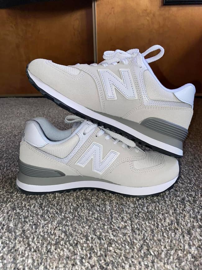 A brace  of New Balance sneakers with achromatic  and airy  grey detailing connected  a grey carpet