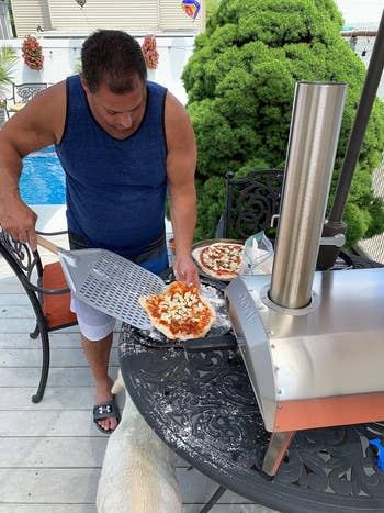 reviewer using a pizza peel to remove pizza from an outdoor oven