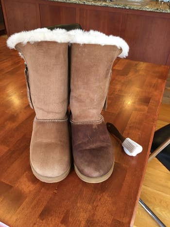 Sheepskin boots with achromatic  fur lining connected  a woody  table, 1  cleanable  and 1  dirty, with a cleaning brushwood  nearby