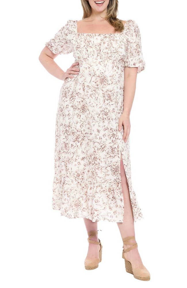 Person wearing a floral-patterned, ankle-length dress with short puff sleeves and side slit, paired with wedge sandals