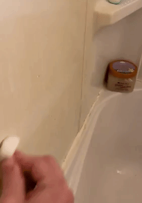 Reviewer using white sponge to clean shower wall