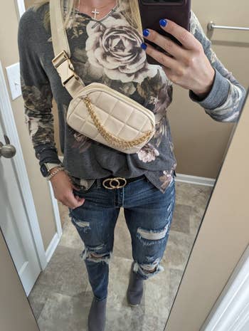 Person in a floral top and distressed jeans showcasing a beige belt bag