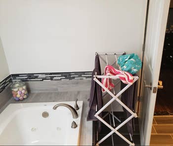 reviewer pic of towels on accordion style drying rack beside tub
