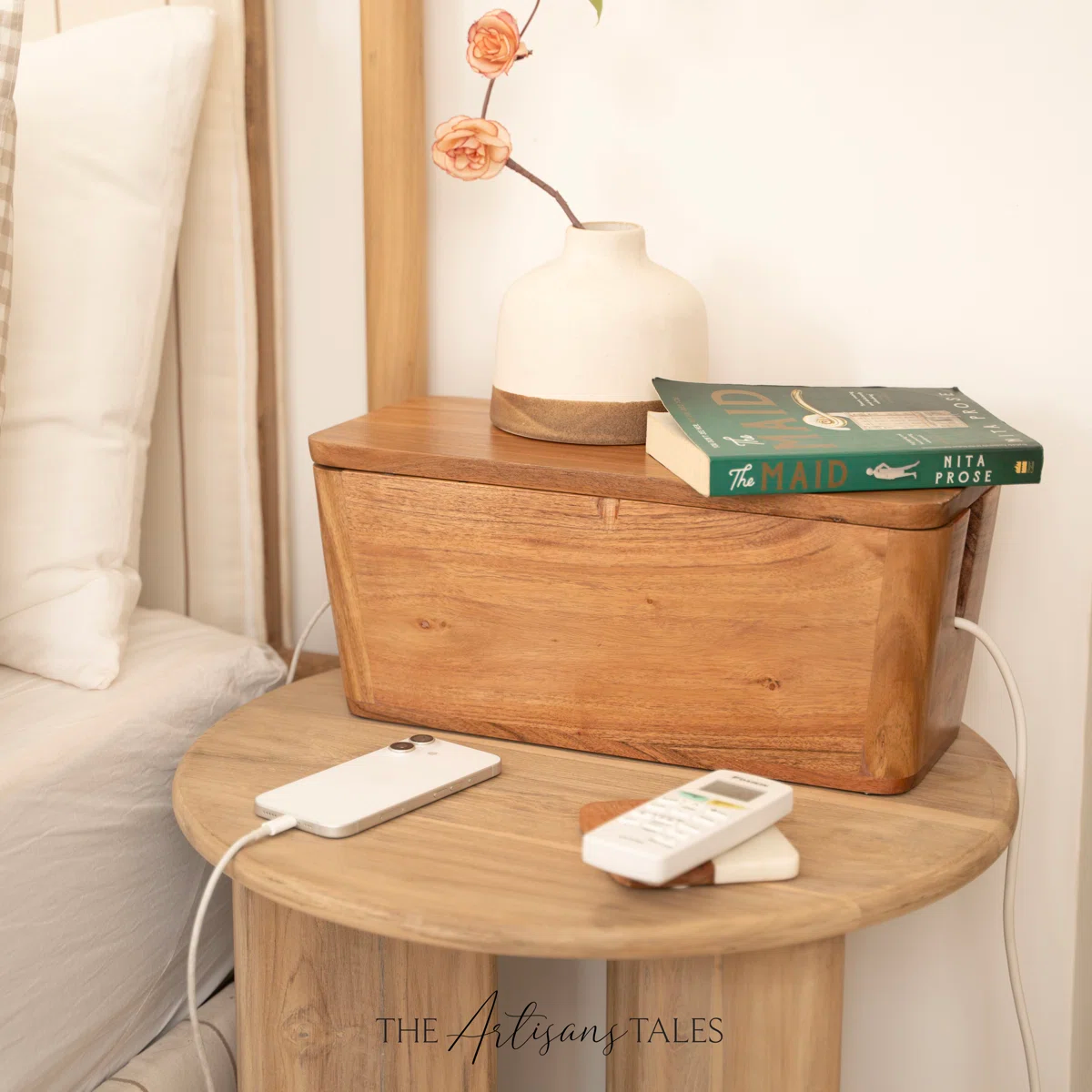 Wooden nightstand with a sleek phone charger, vase with flowers, and books, creating a cozy, minimalist bedroom atmosphere