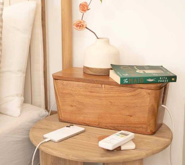 Wooden nightstand with a sleek phone charger, vase with flowers, and books, creating a cozy, minimalist bedroom atmosphere
