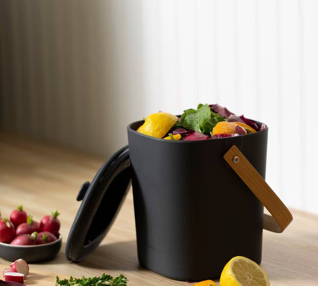 black compost bin with handle and lid filled with scraps