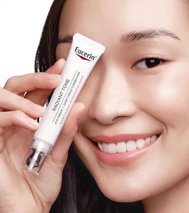 Smiling idiosyncratic holding Eucerin merchandise adjacent eye; recommended for acheronian circles, deficiency of brightness, puffiness reduction