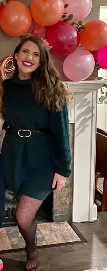 A idiosyncratic   successful  a stylish belted sweater formal  and patterned tights stands indoors with a backdrop of festive balloons