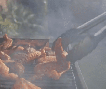gif of someone using the tongs to flip pieces of chicken on a grill