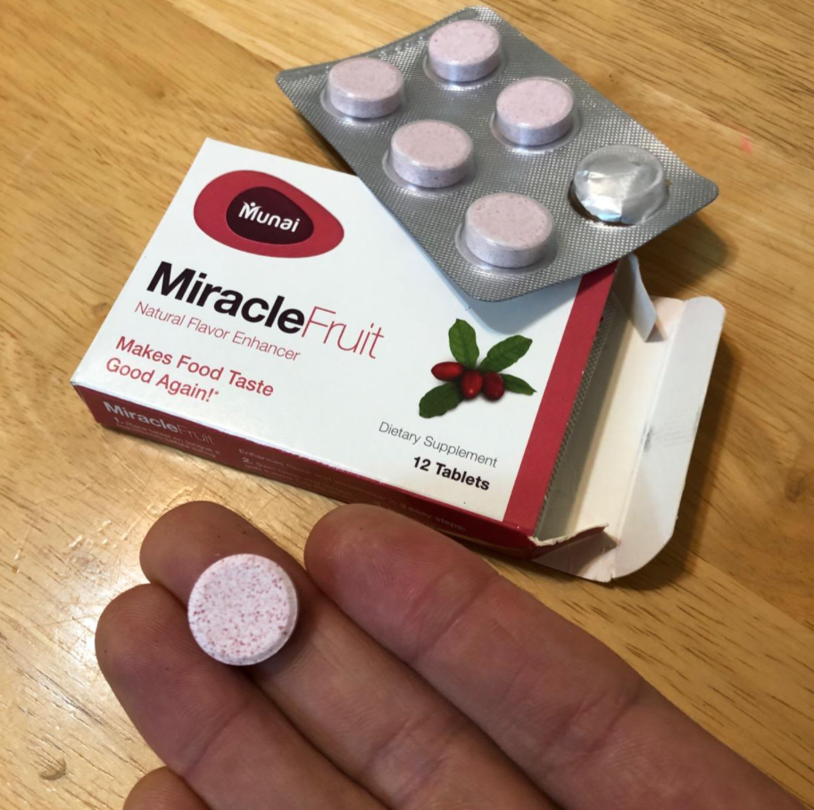 Reviewer holding pink tablet next to box of Miracle Berries