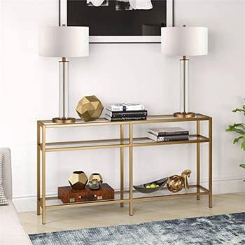 a gold console table holding lamps and decor