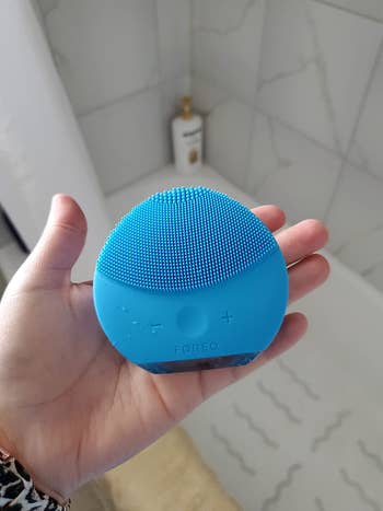 reviewer photo of them holding a blue sonic cleansing brush