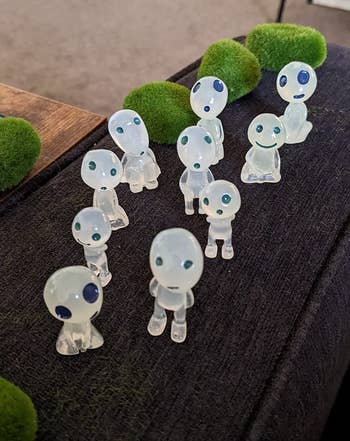 Small transparent figurines on a surface with mossy decorations
