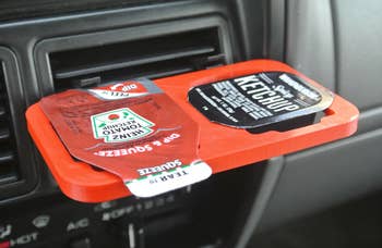 Close up of a container of two different ketchups in the double clip holder attached to a car vent