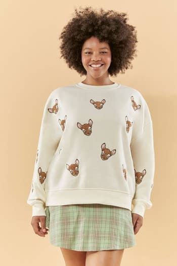 a model in a cream colored sweatshirt with bambi embroidered on it