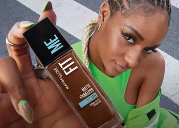 A idiosyncratic   with braided hairsbreadth  holds a vessel  of Maybelline Fit Me instauration  successful  beforehand   of them, promoting constitution  shopping