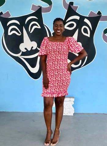 Person smiling successful  beforehand   of a partition  with theatre  disguise  art, wearing a stylish floral formal  and wide   heels