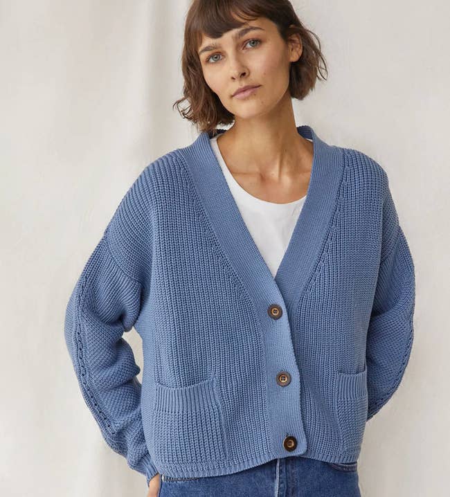 A model wearing a blue cardigan with pockets and buttons