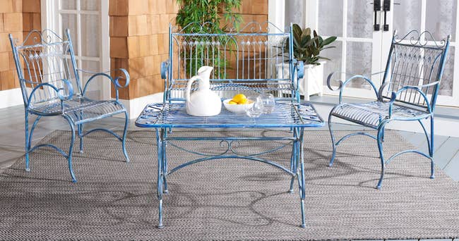 Blue antique-styled wrought iron loveseat and chairs around a matching rectangular table outside on a rug