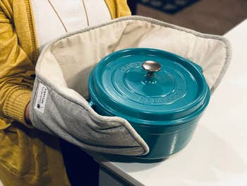 someone using the gray double oven mitt to carry a dutch oven