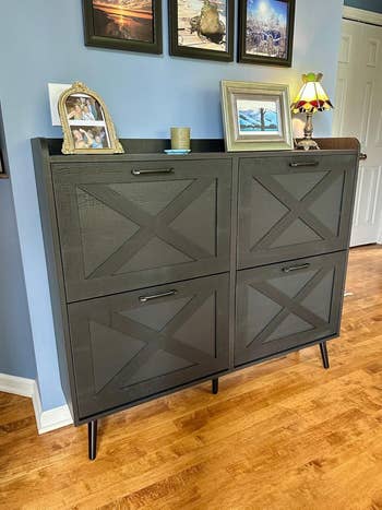 Shoe cabinet with four compartments and a ledge holding framed photos and a small lamp in a home setting
