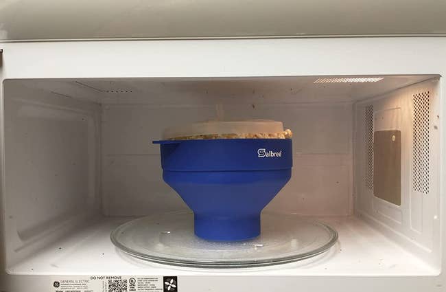 reviewer image of the blue bowl with clear lid in a microwave full of fully popped popcorn