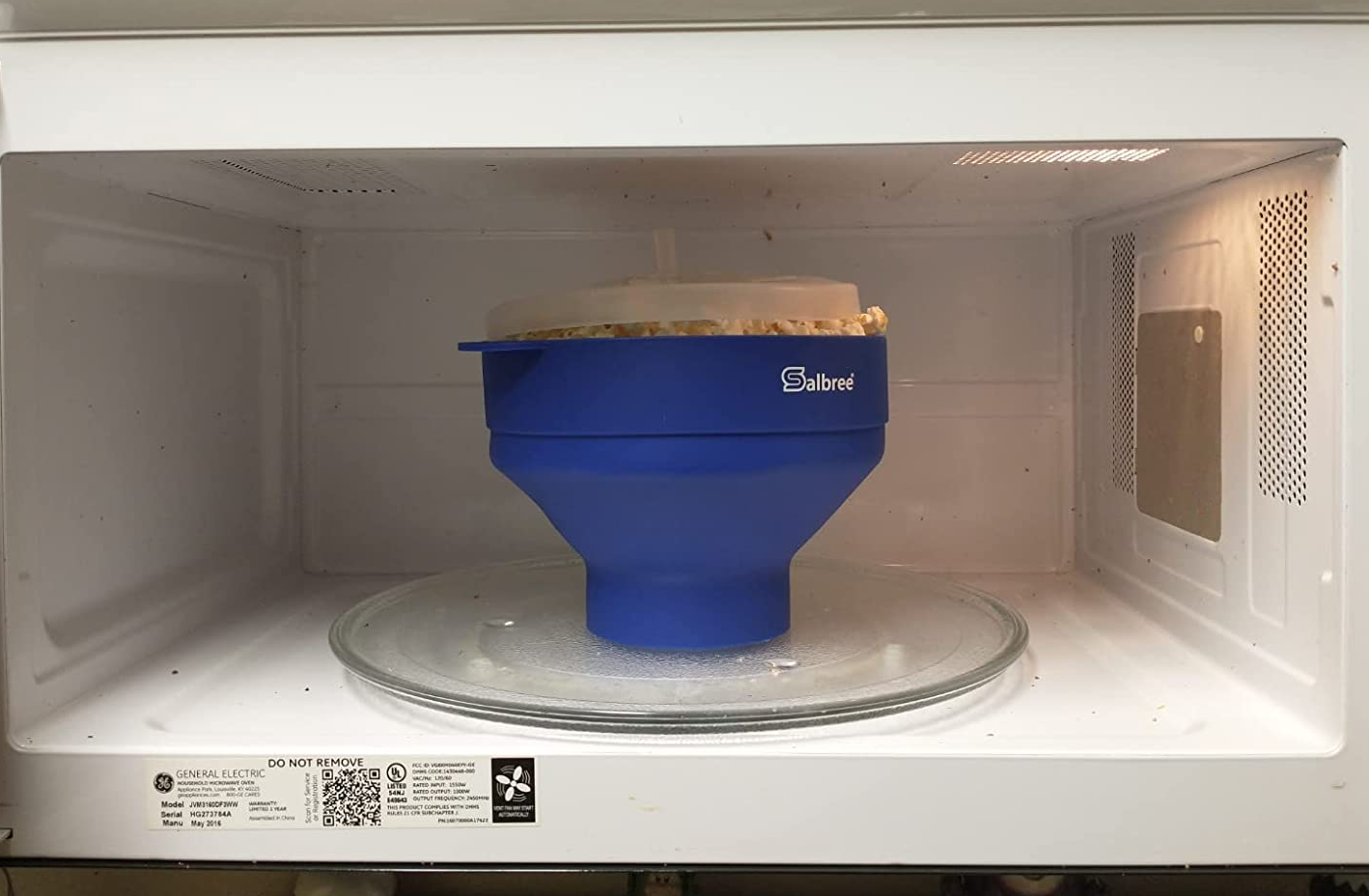 reviewer image of the blue bowl with clear lid in a microwave full of fully popped popcorn