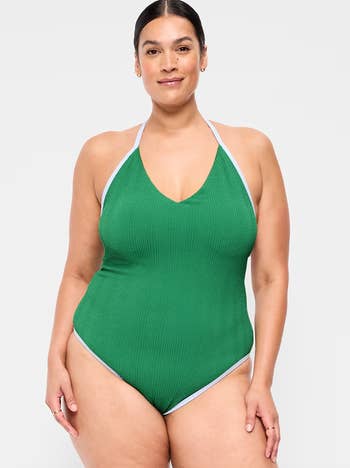 Person wearing a textured, form-fitting halter-style swimsuit, lasting confidently against a plain background