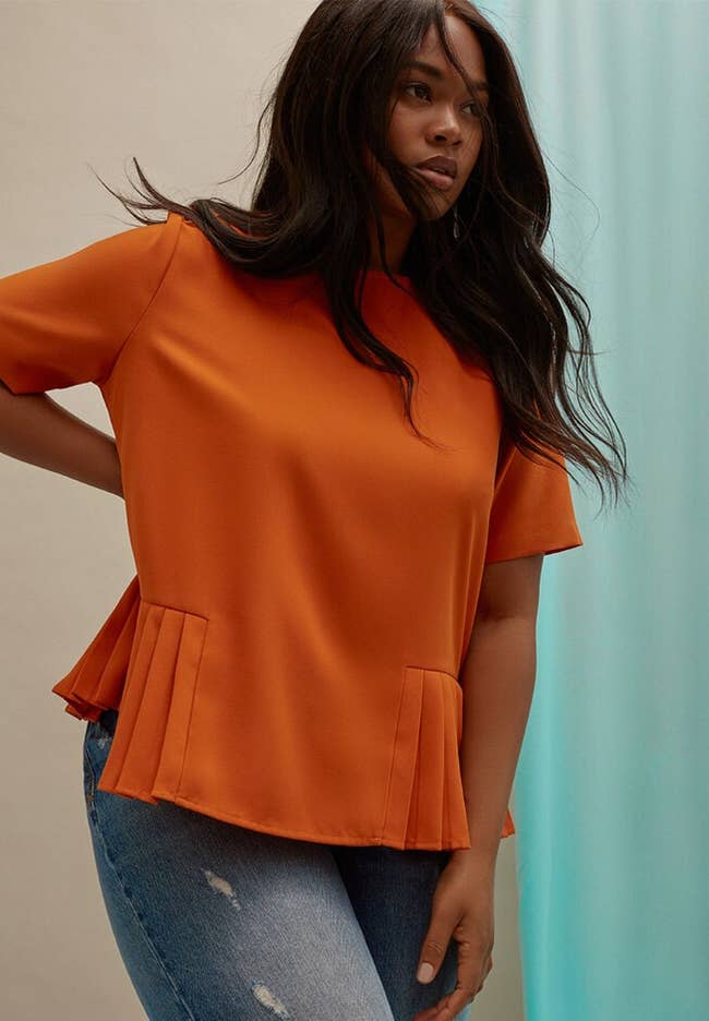 Model in orange peplum top and jeans posing