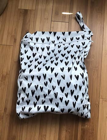 a reviewer photo of a travel laundry bag in white featuring a black heart print 