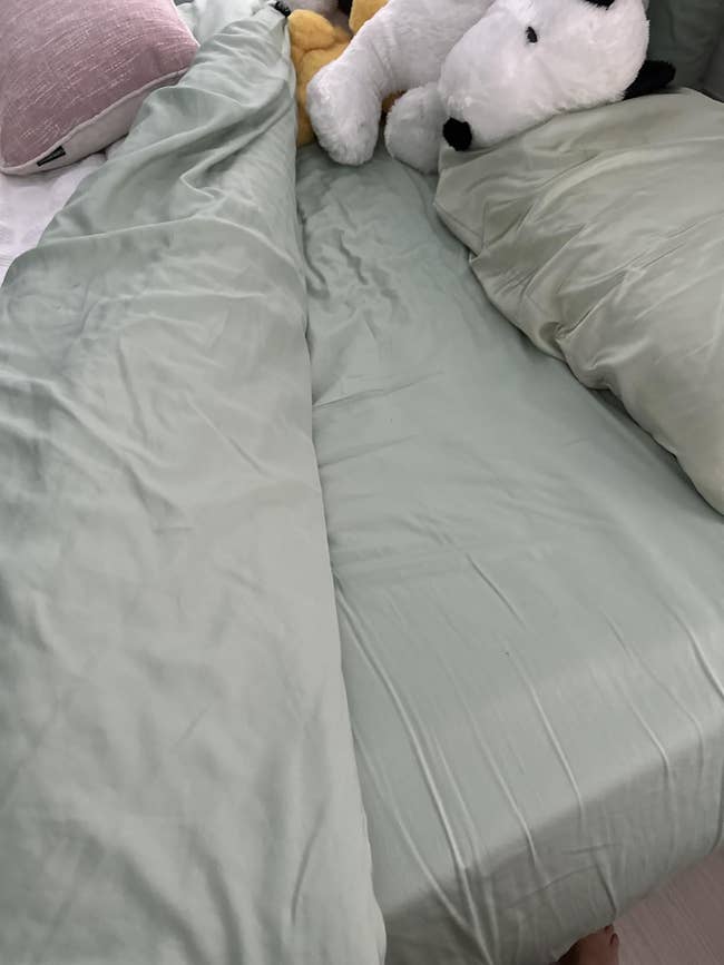 Unmade furniture with airy sheets and plush toys, including a ample stuffed carnal adjacent pillows
