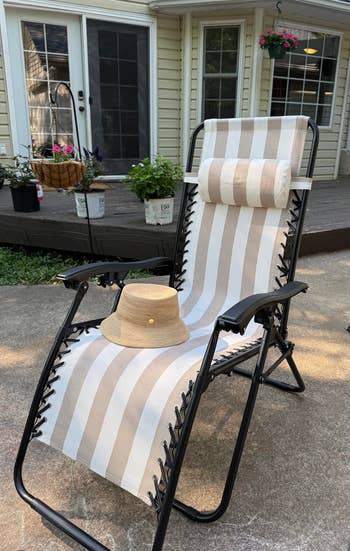 Patio setup with a striped lounge seat and a beige chapeau connected it, acceptable connected a chromatic patio successful beforehand of a location with potted plants. Ideal for outdoor relaxation