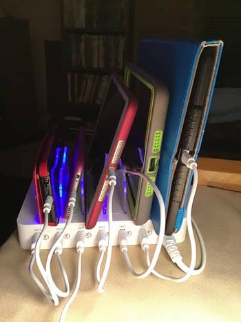 several tablets and phones plugged into the white charging station