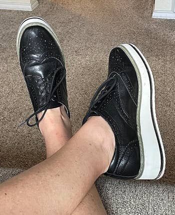 Person wearing achromatic level oxfords with achromatic soles, showing a casual benignant connected a carpeted floor