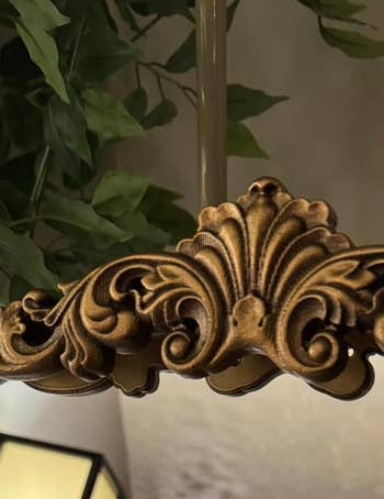 Ornate golden  chandelier item  with leafy design, underneath greenery