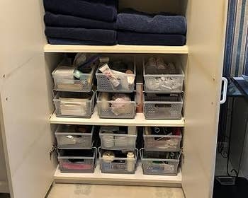 Organized bath closet with towels and wide bins storing toiletries and cleaning supplies connected shelves