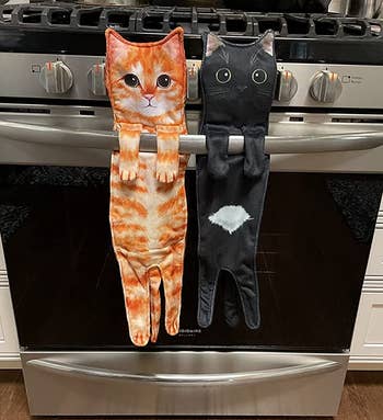 an orange cat towel and a black cat towel hanging from a reviewer's oven door