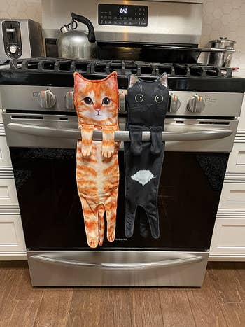 an orangish  feline  towel and a achromatic  feline  towel hanging from a reviewer's oven door
