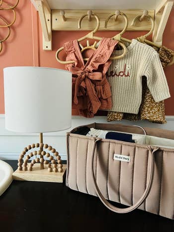 Nursery decor with a modern lamp and neutral-colored baby clothes on hangers, along with a beige diaper bag
