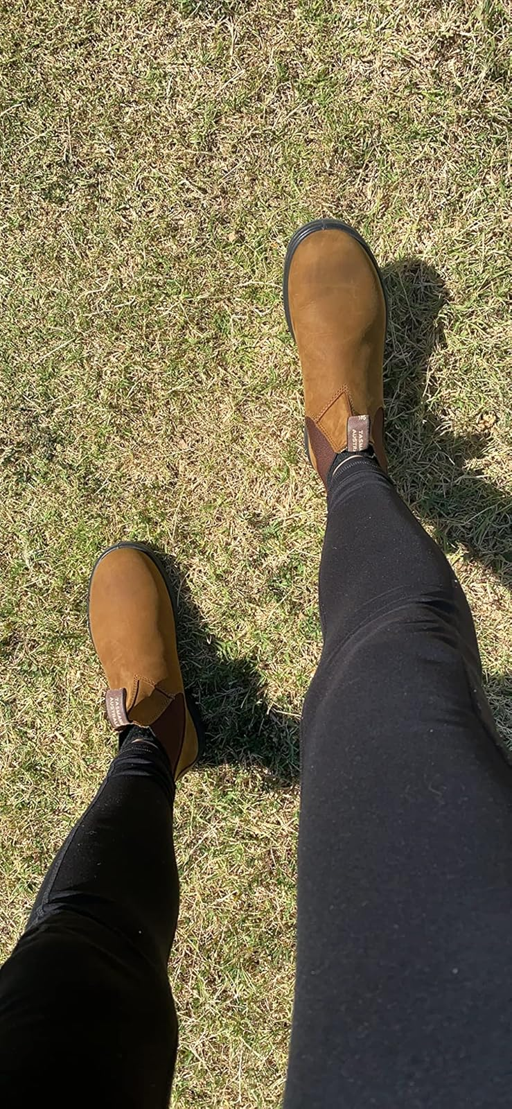 Person wearing brownish  ankle boots and achromatic  leggings lasting  connected  grass, showcasing a casual outdoor style