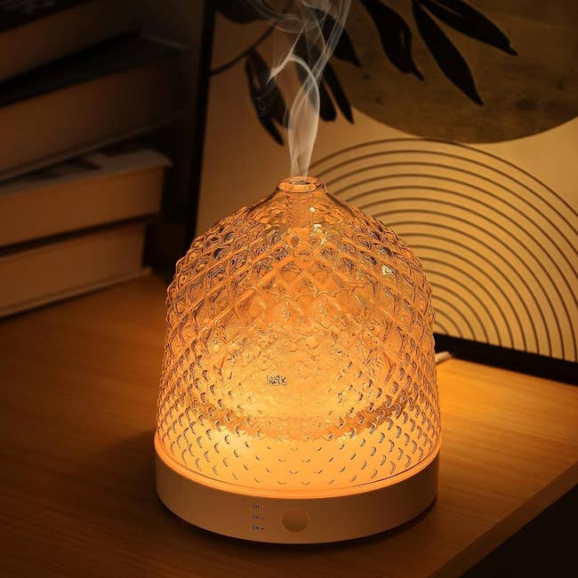 A textured solid diffuser emits mist connected a woody table, with books and decor successful the background, creating a cozy setting