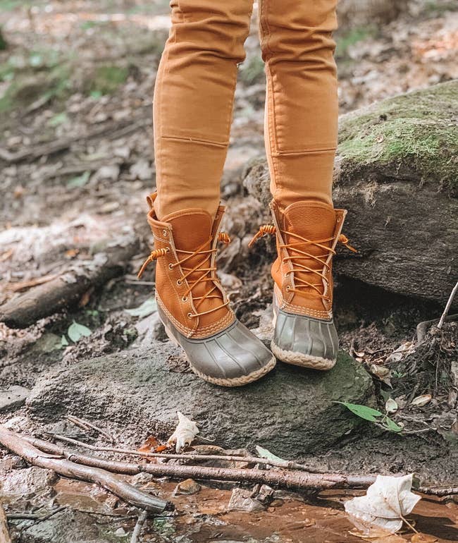 A person is wearing the tan duck boots while standing on a small rock