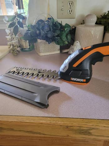 A reviewer's cordless hedge trimmer rests on a countertop with its blade guard off to the side