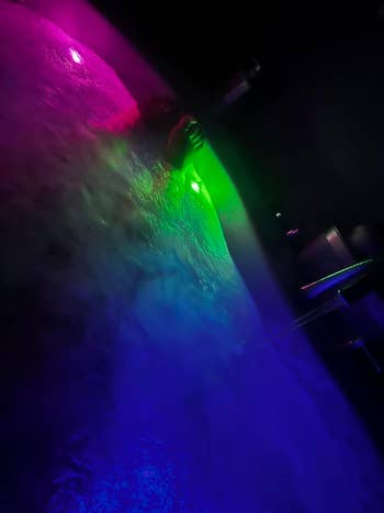 Person in a bathtub glowing various colors from the bath fizzes
