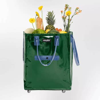 Green buying container connected wheels, filled with groceries similar bread, pineapple, and flowers, highlighting its capableness and convenience for shoppers