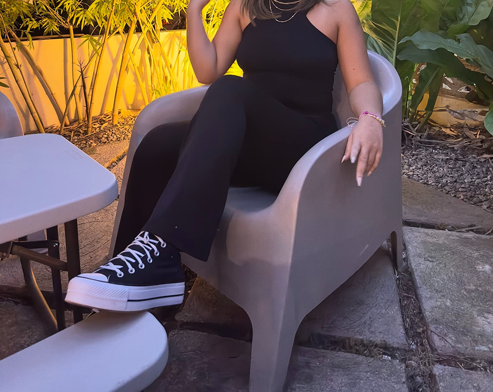 Person sitting outside, wearing a sleeveless outfit and high-top sneakers, with casual yet stylish flair