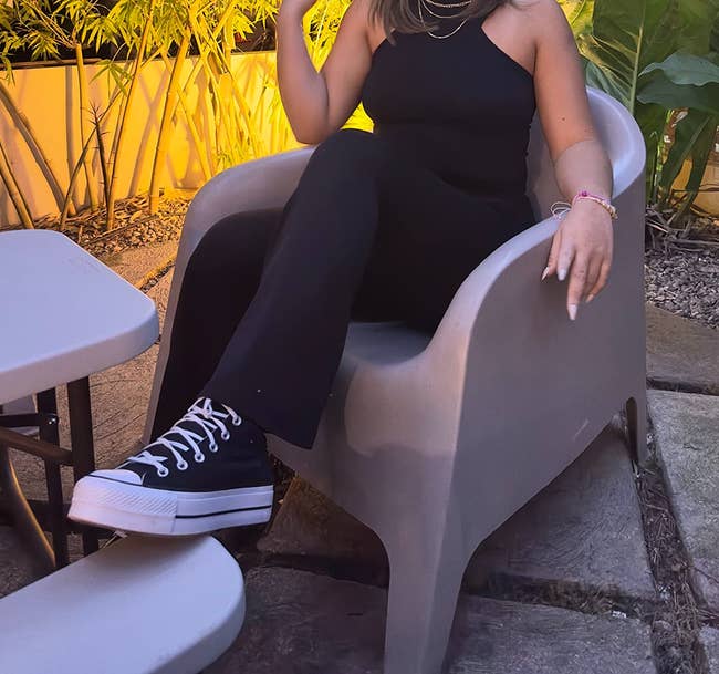 Person sitting outside, wearing a sleeveless outfit and high-top sneakers, with casual yet stylish flair