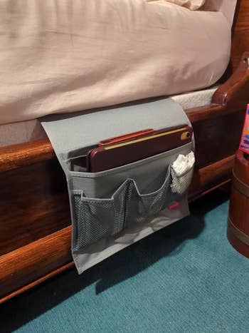 Bedside cloth organizer with pockets holds a smartphone and tissue, attached to a bedframe, convenient for nighttime storage