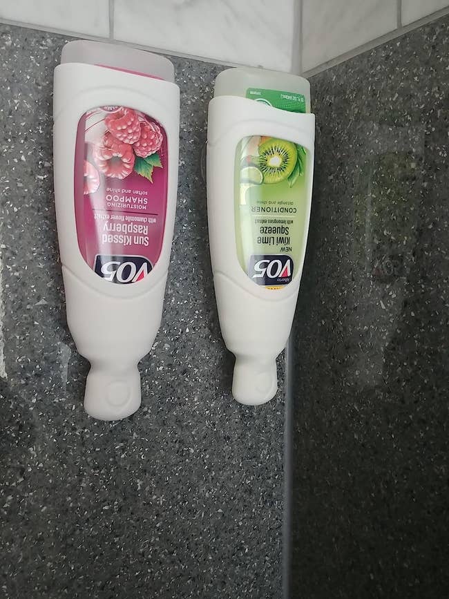Two of the silicone dispensers in white holding shampoos in a shower